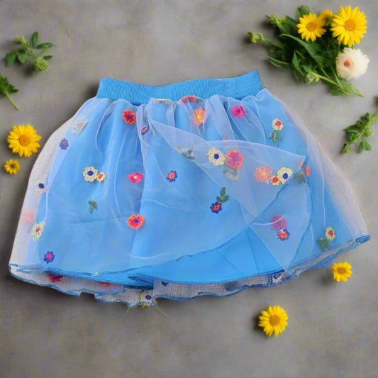 Blue skirt with floral embroidery on a gray surface with yellow flowers.