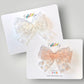 Two decorative bows on white display cards against a light gray background. The top bow is white lace with small embroidered snowflakes.  The bottom bow is blush lace with small embroidered snowflakes.
