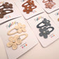 Six flower-shaped hair clips in assorted earthy colors, each attached to a white display card.