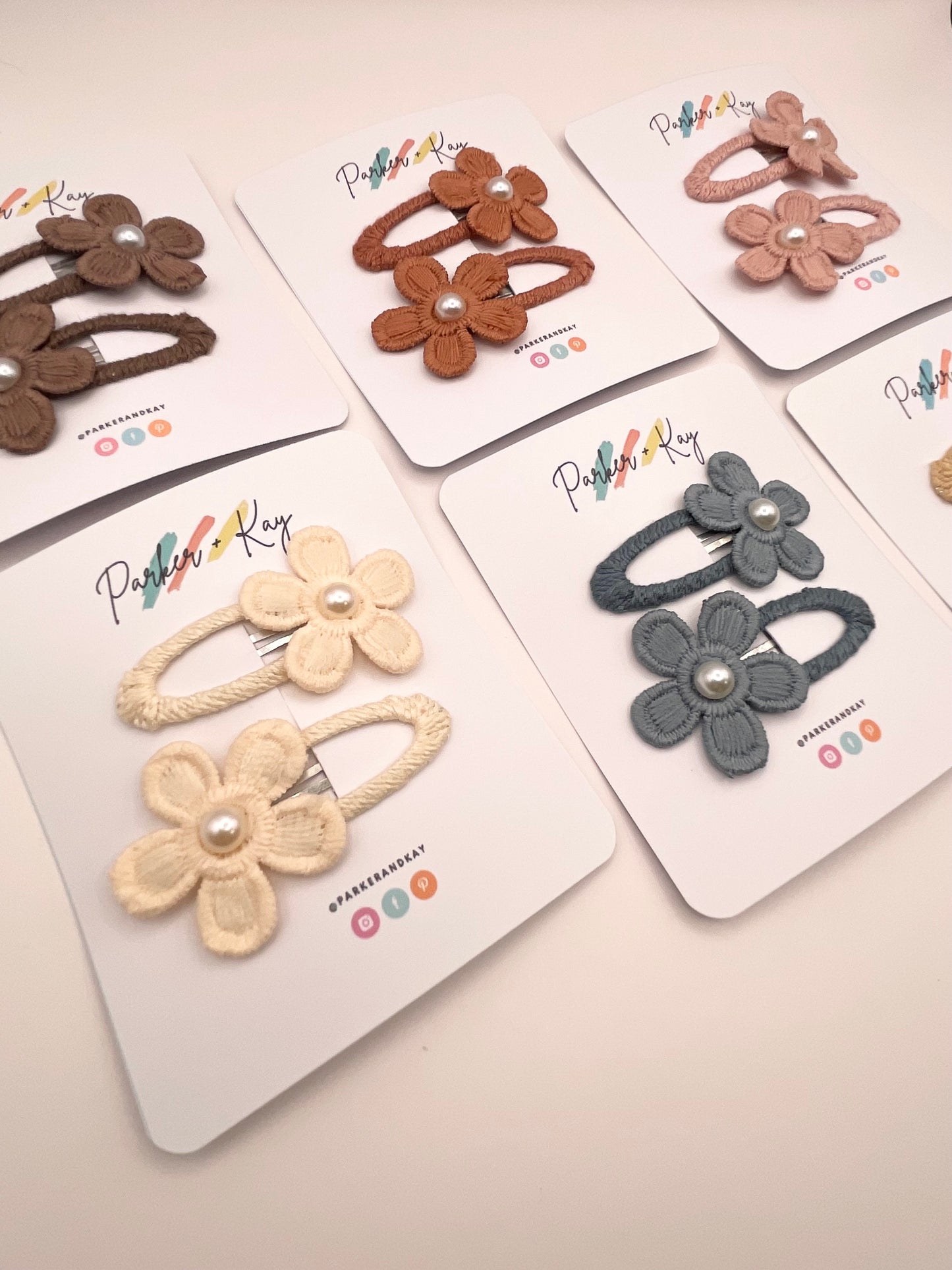 Six flower-shaped hair clips in assorted earthy colors, each attached to a white display card.