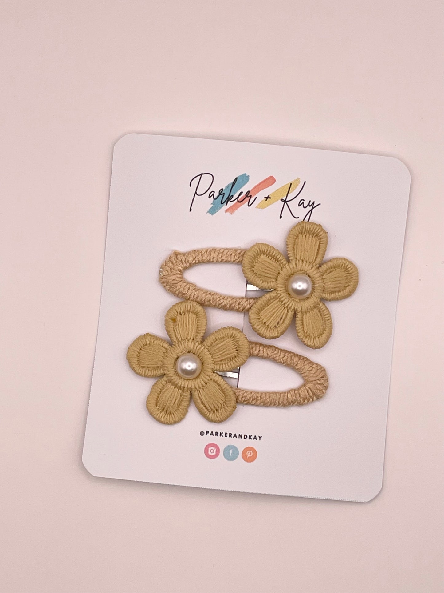 Two golden yellow hair clips with embroidered flower details and pearl centers, displayed on a white branded card that reads Parker + Kay.