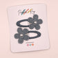 Two bluish-gray fabric flower hair clips with pearl centers, attached to a white display card printed with the brand name 'Parker & Kay'.