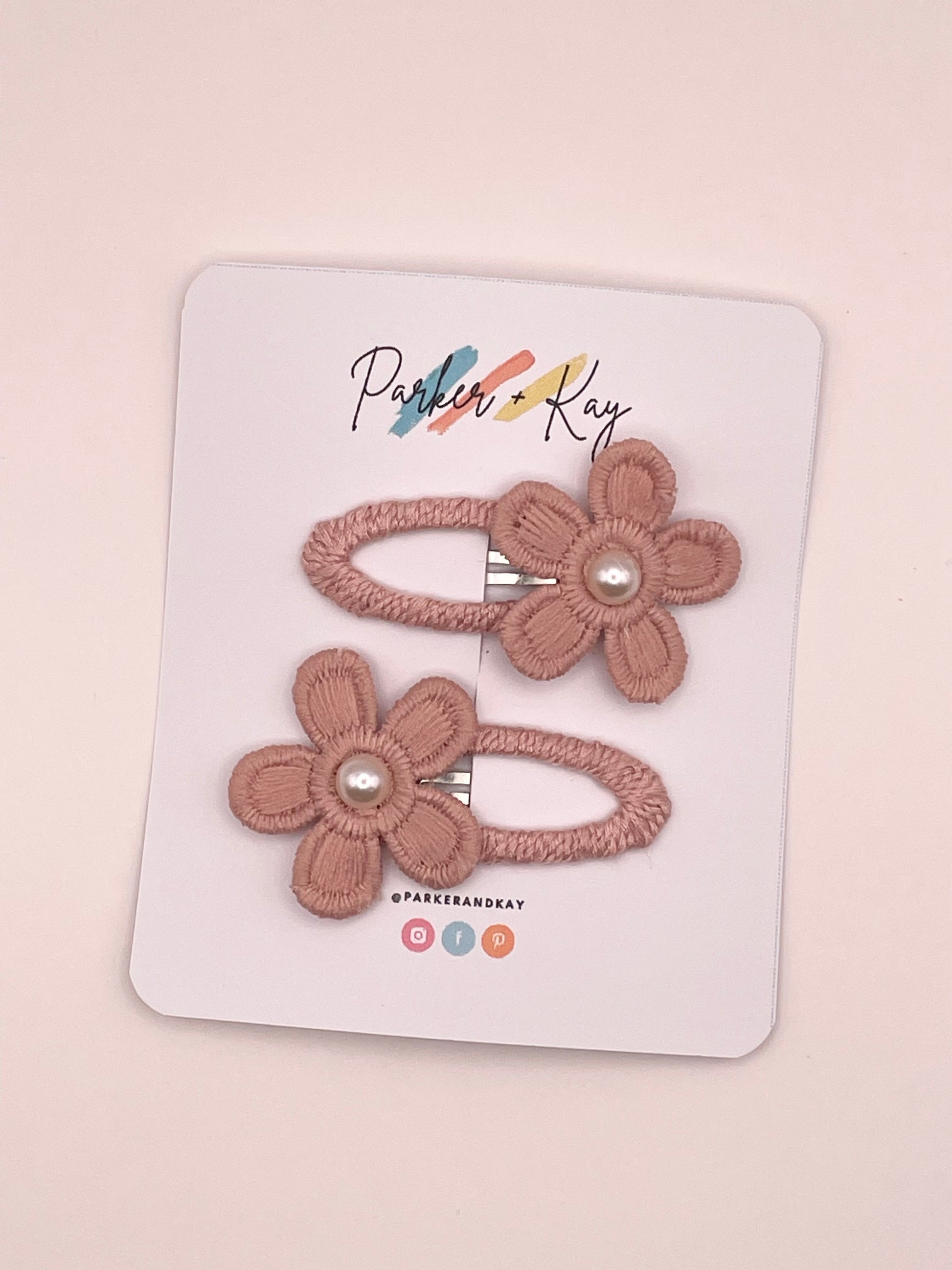 Two dusty pink flower-shaped hair clips with pearl centers, displayed on a white branded card that reads Parker & Kay.