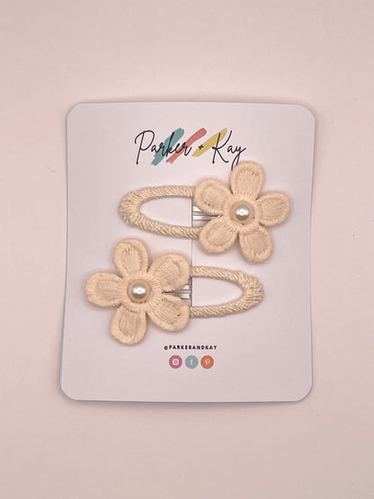 Two cream-colored fabric flower hair clips with pearl centers, attached to a white display card branded 'Parker + Kay'.