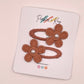 Two terracotta embroidered flower hair clips with pearl centers, attached to a white display card branded Parker & Kay.