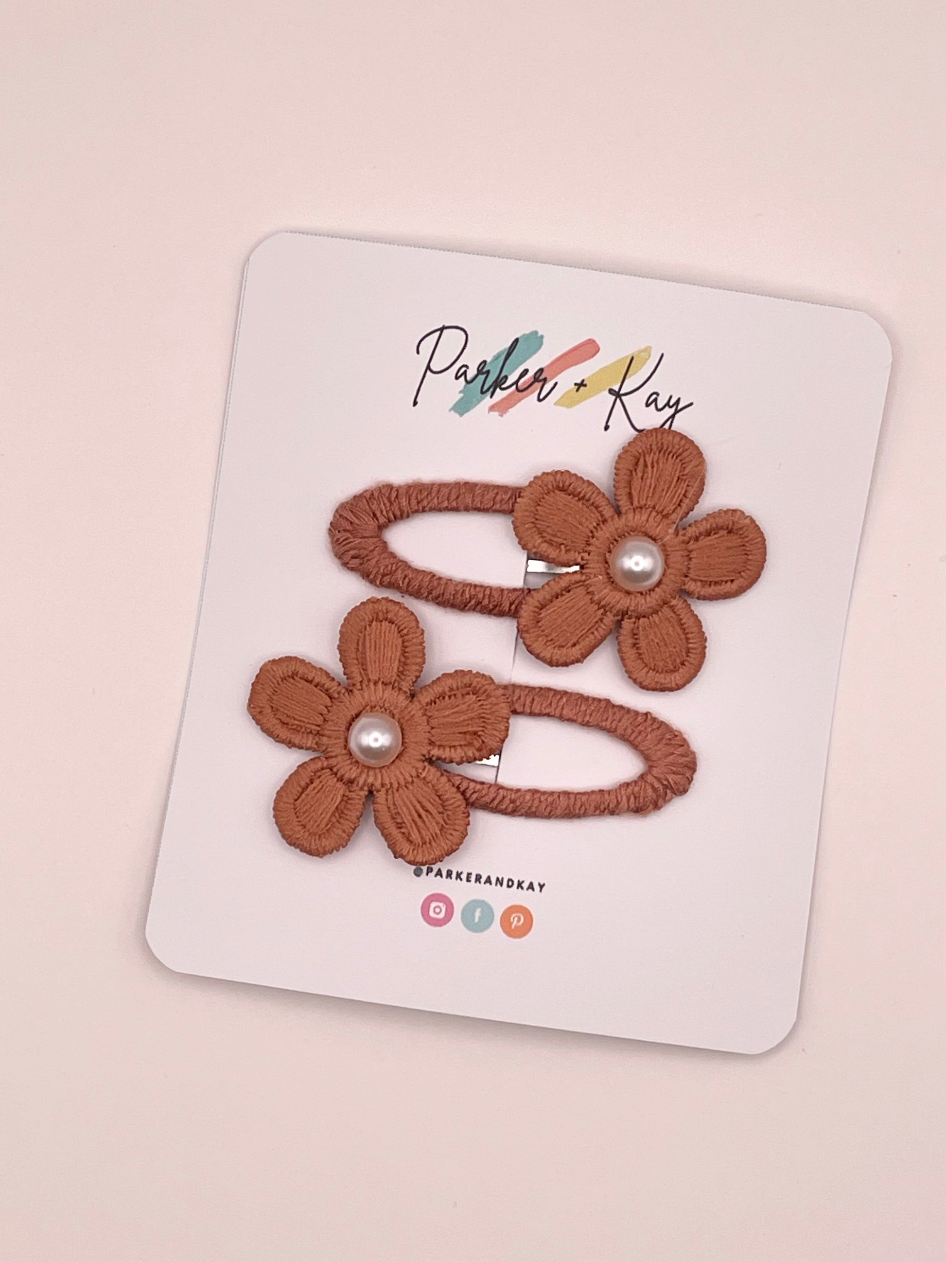 Two terracotta embroidered flower hair clips with pearl centers, attached to a white display card branded Parker & Kay.