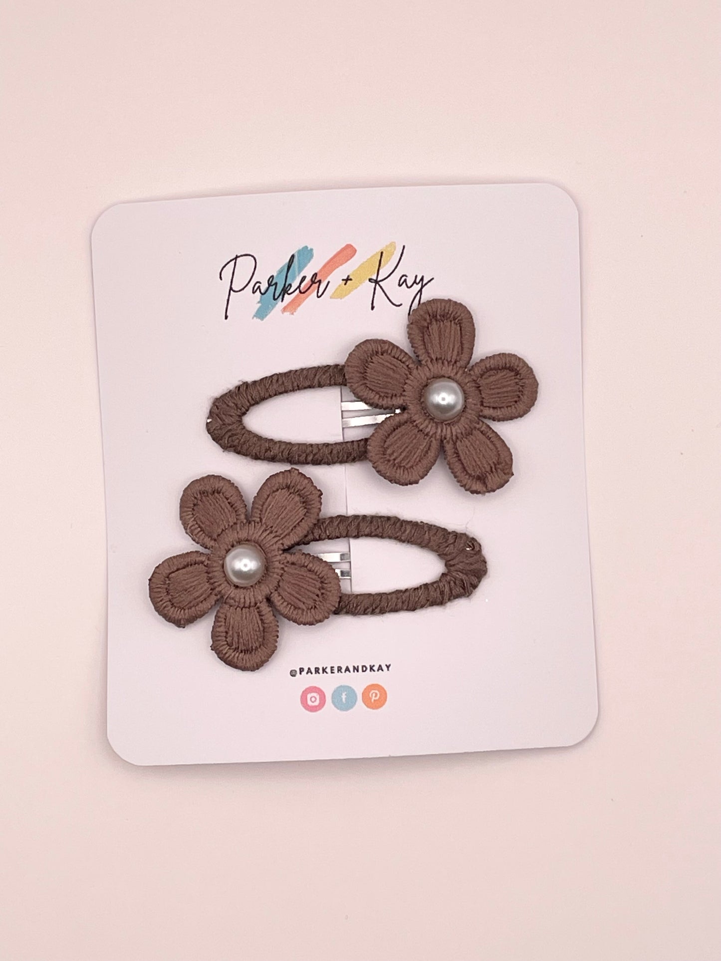 Two brown fabric flower hair clips with pearl centers, attached to a white display card branded Parker & Kay.