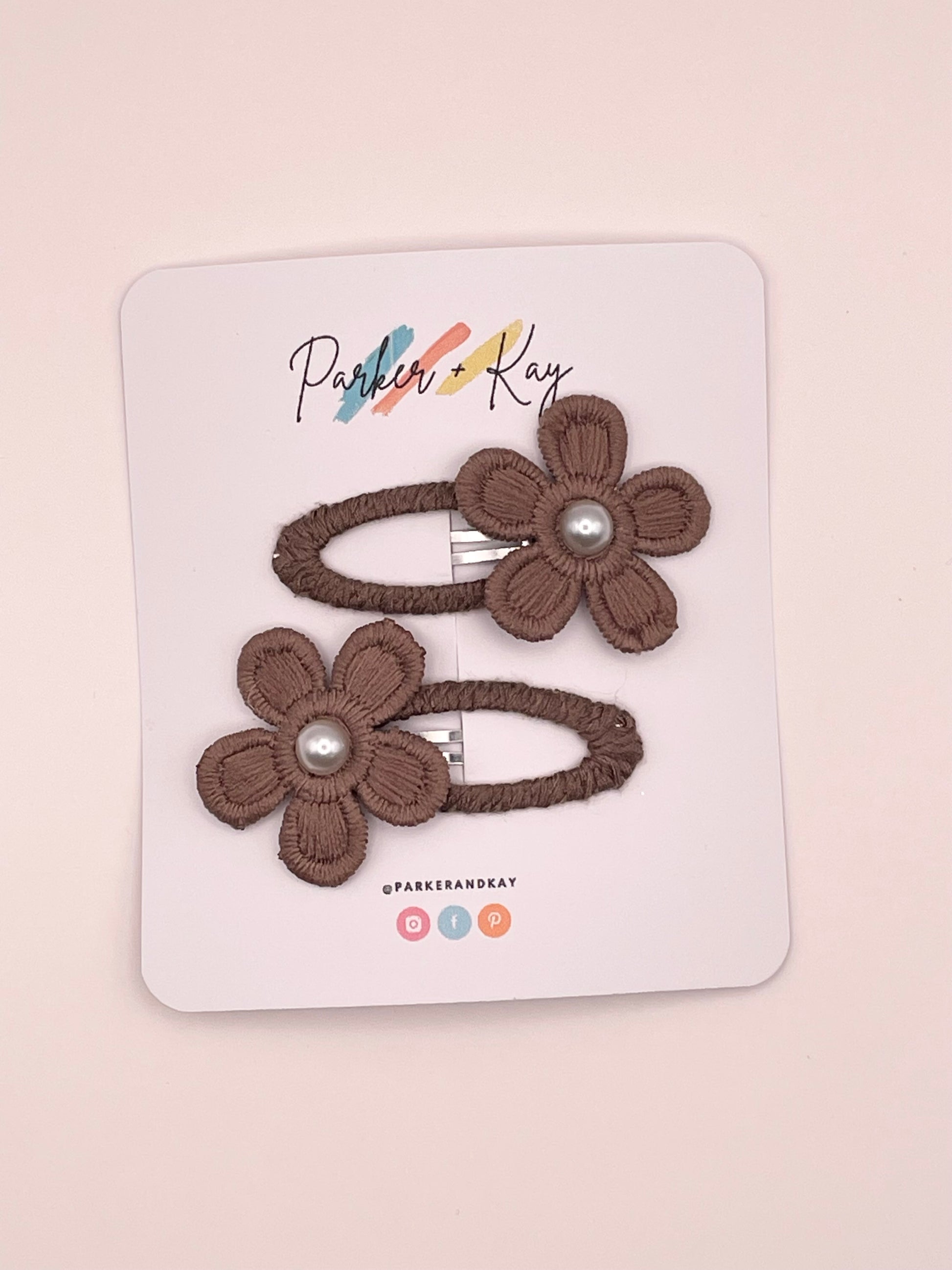 Two brown fabric flower hair clips with pearl centers, attached to a white display card branded Parker & Kay.